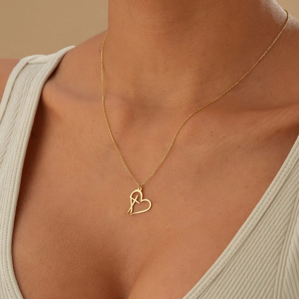 14k Gold heart-shaped cross necklace on a person wearing a beige top against a beige background