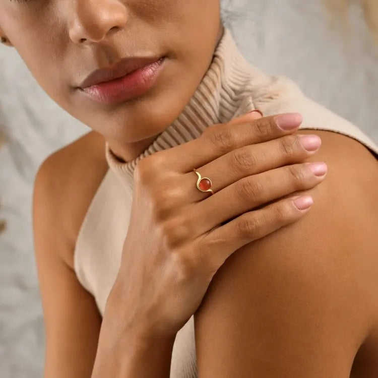 Woman model wearing a 14k gold filled ring with a light red carnelian gemstone on her hand, against a neutral background.