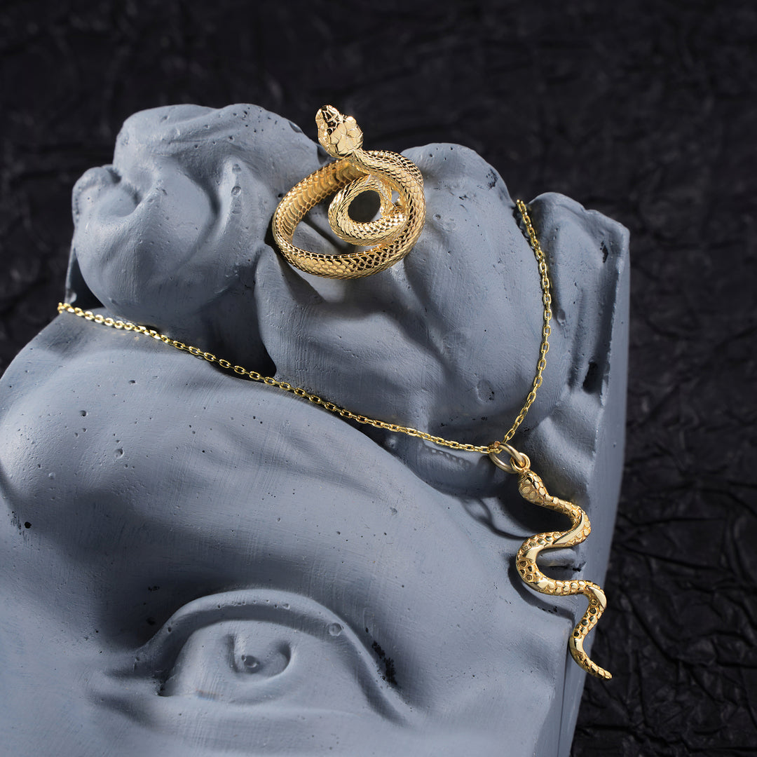 Gold snake necklace on a gray stone surface with a dark textured background