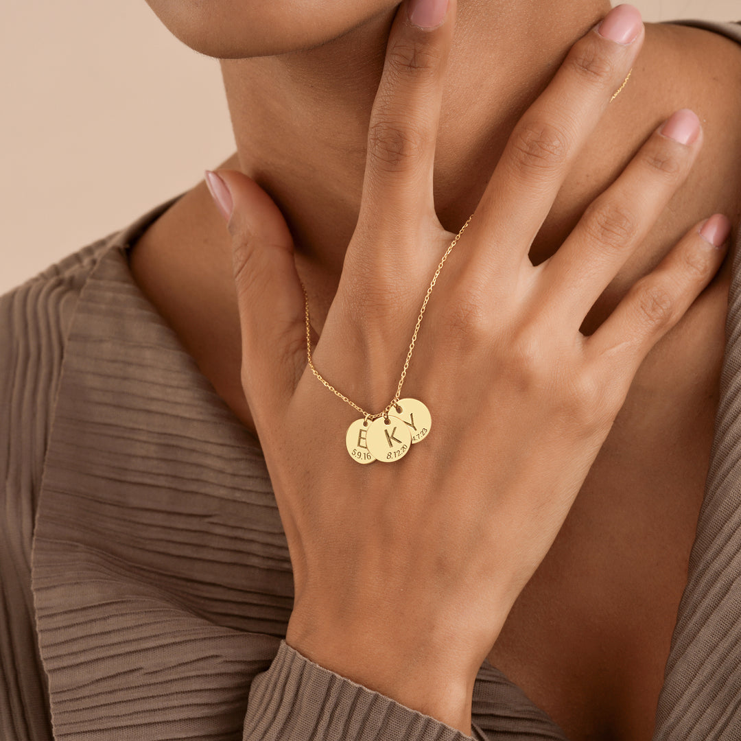 Gold necklace with round pendants on a person's hand against a beige background
