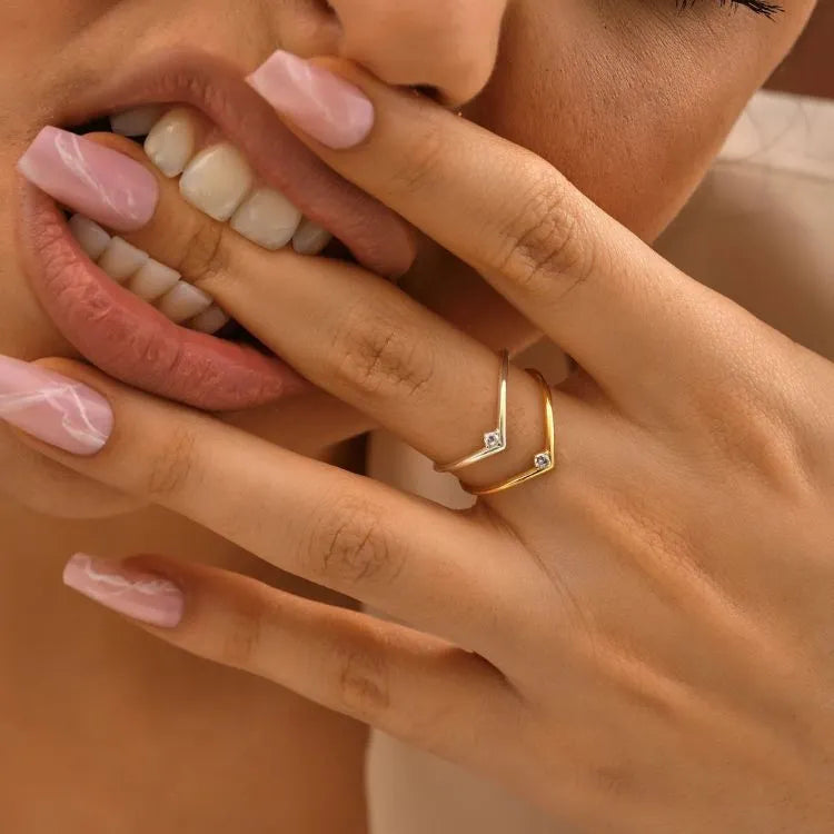 Close-up of a hand with pink nail polish and a 14k gold filled diamond chevron ring, covering part of a person's face.