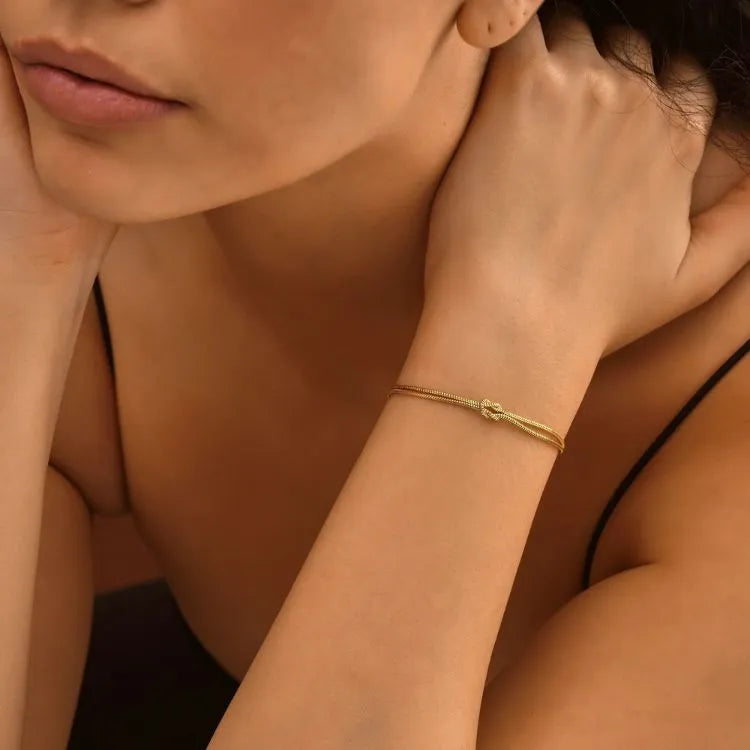 Close-up of a woman's arm with a 14k gold filled knot bracelet against a warm-toned background