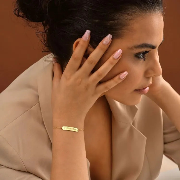 Woman model wearing a 14k gold filled bracelet with a name charm against a brown background