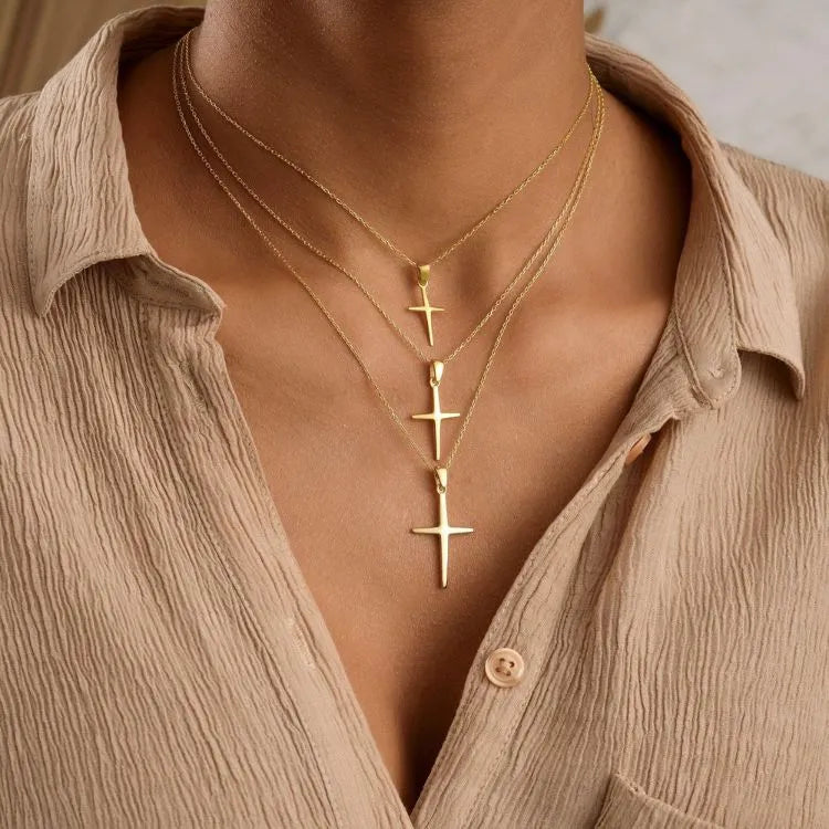 Three 14k Gold filled cross necklaces with differenc chain lengths on a person wearing a beige shirt