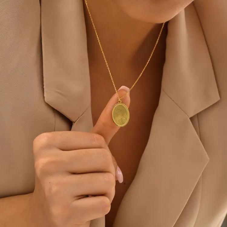 Woman model wearing a 14k gold filled necklace with an fingerprint engraved oval pendant, set against a neutral background.