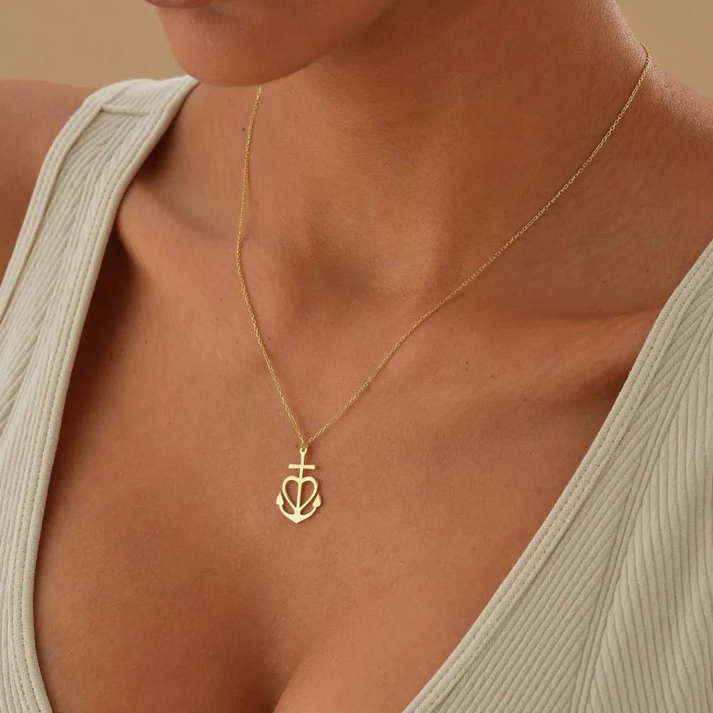 14k Gold necklace with a heart and anchor pendant on a person wearing a beige top.