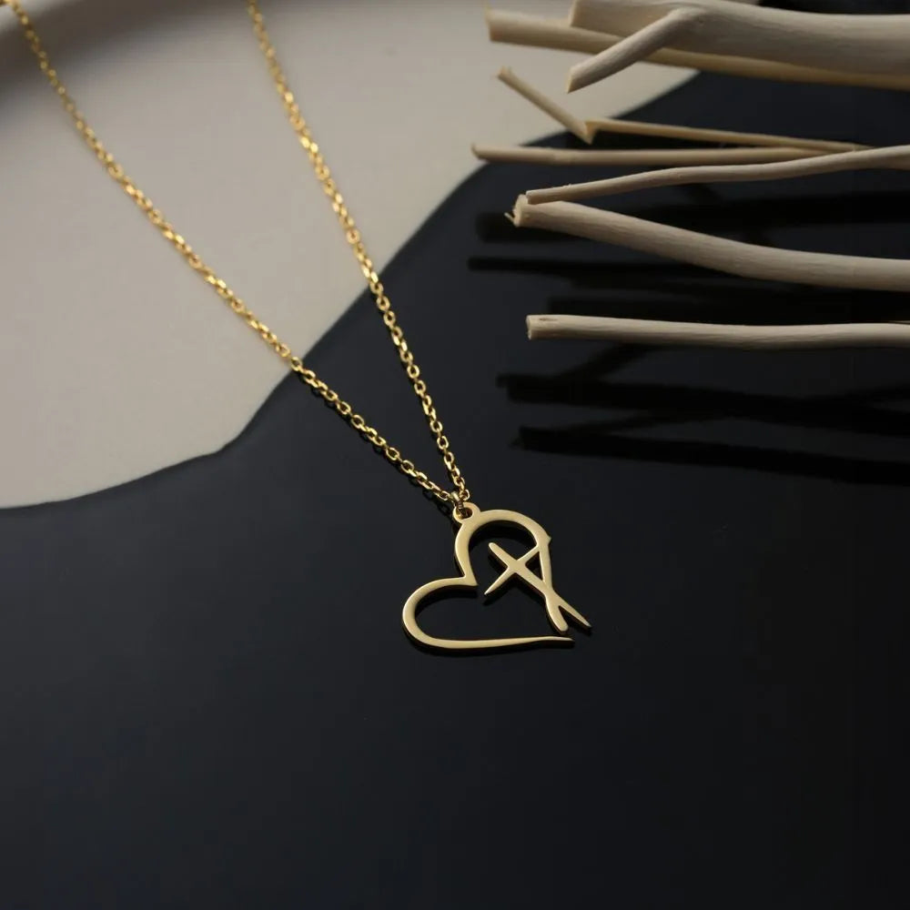 14k Gold necklace with an outlined heart and cross shaped pendant on a dark surface