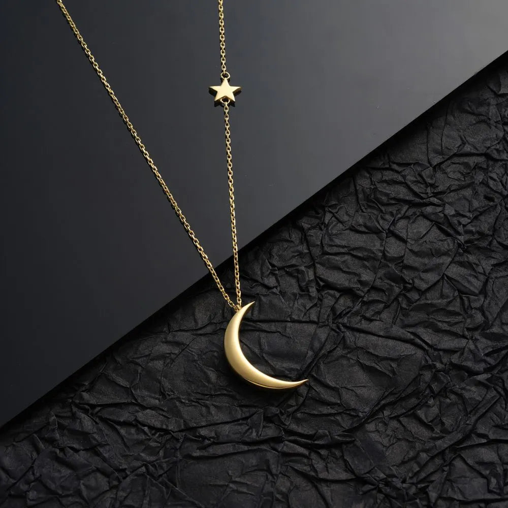 14k Gold necklace with a star and moon pendant on a black textured background