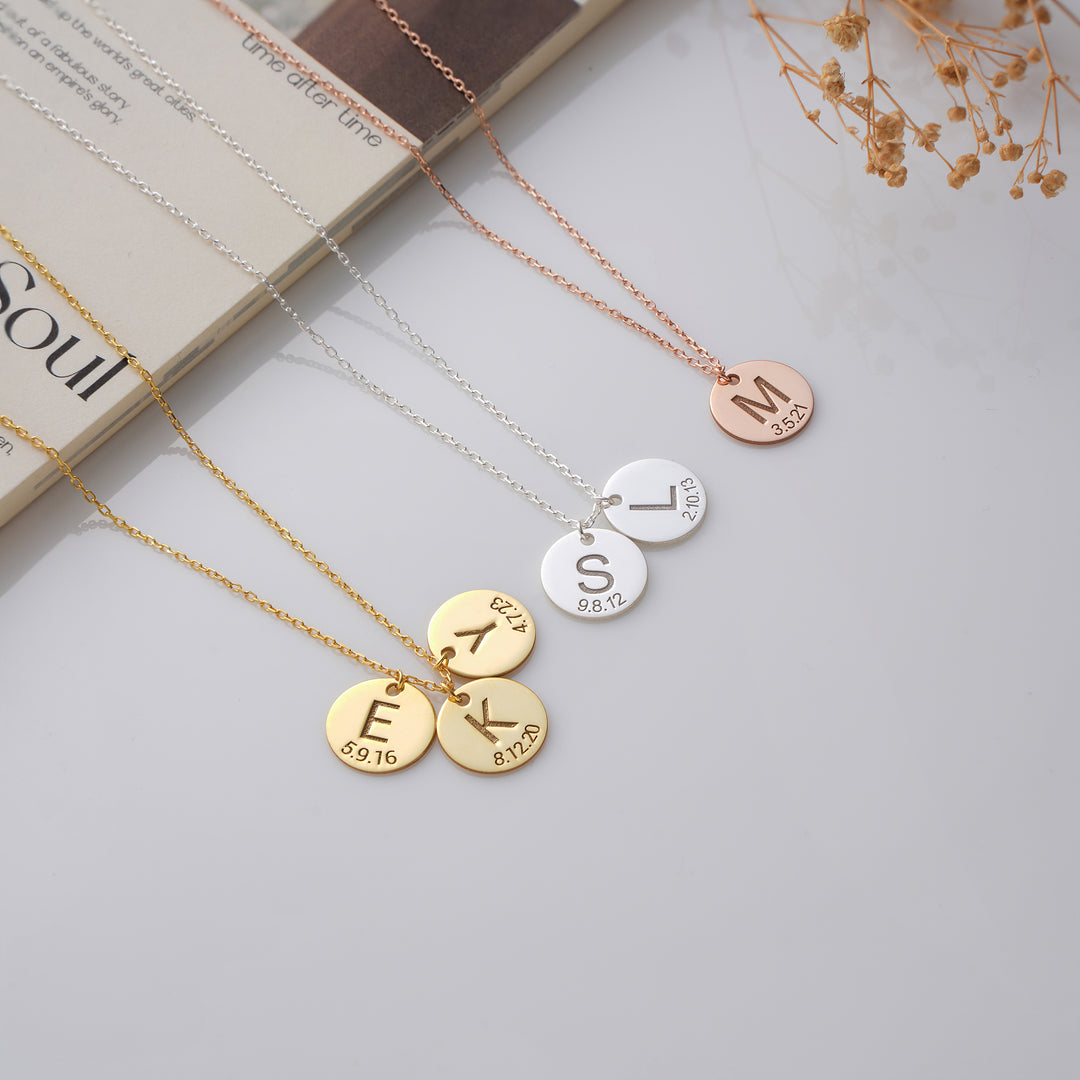 Three necklaces with round pendants displaying initials on a light surface.