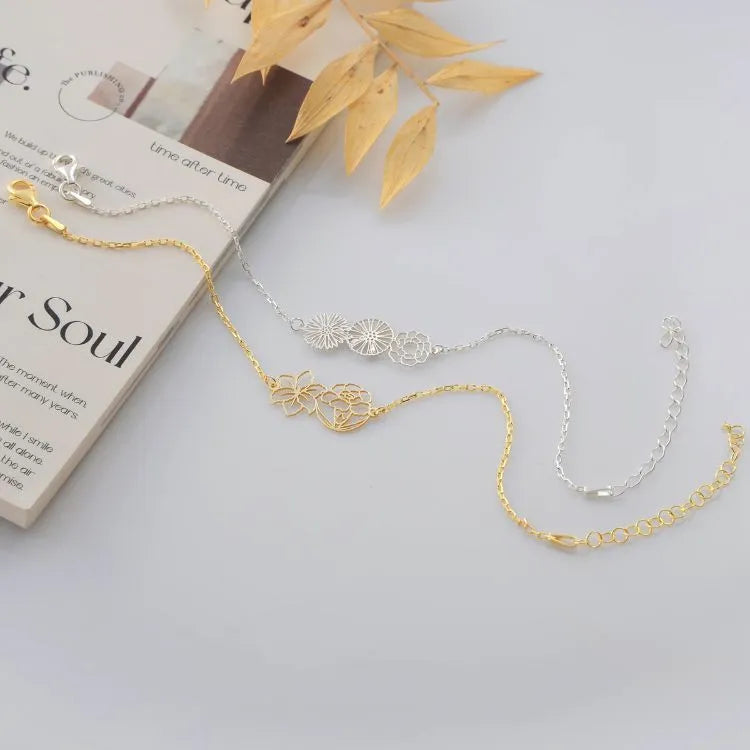 14k gold filled and sterling silver cut out birth flower bracelets on a light surface with a book and leaves in the background.
