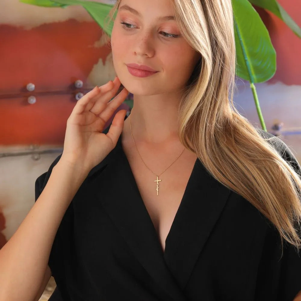Young woman wearing a 14k gold necklace with a cross pendant in front of a colorful background