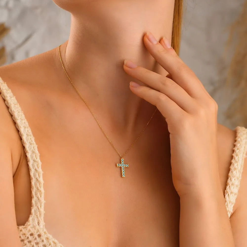 Woman model wearing a 14k gold necklace with a cross pendant, hand touching neck