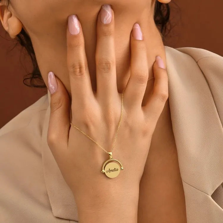 14k Gold filled necklace with a pendant on a hand with pink nail polish against a brown background