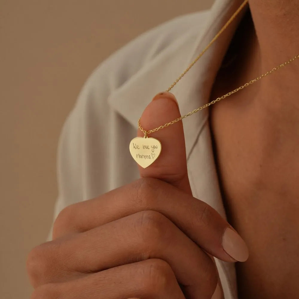 14k Gold heart-shaped necklace with engraved text on a neutral background