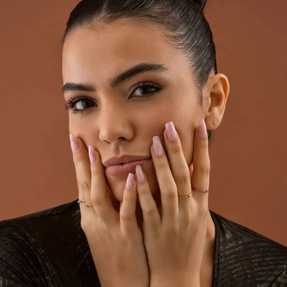Woman with hands on face against a brown background, wearing mini birthstone rings