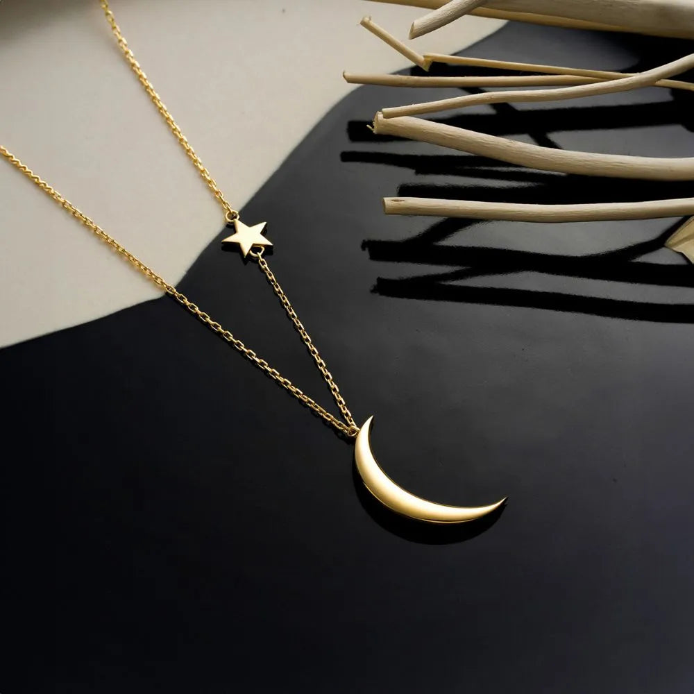 14k Gold necklace with a crescent moon and star pendant on a dark surface.