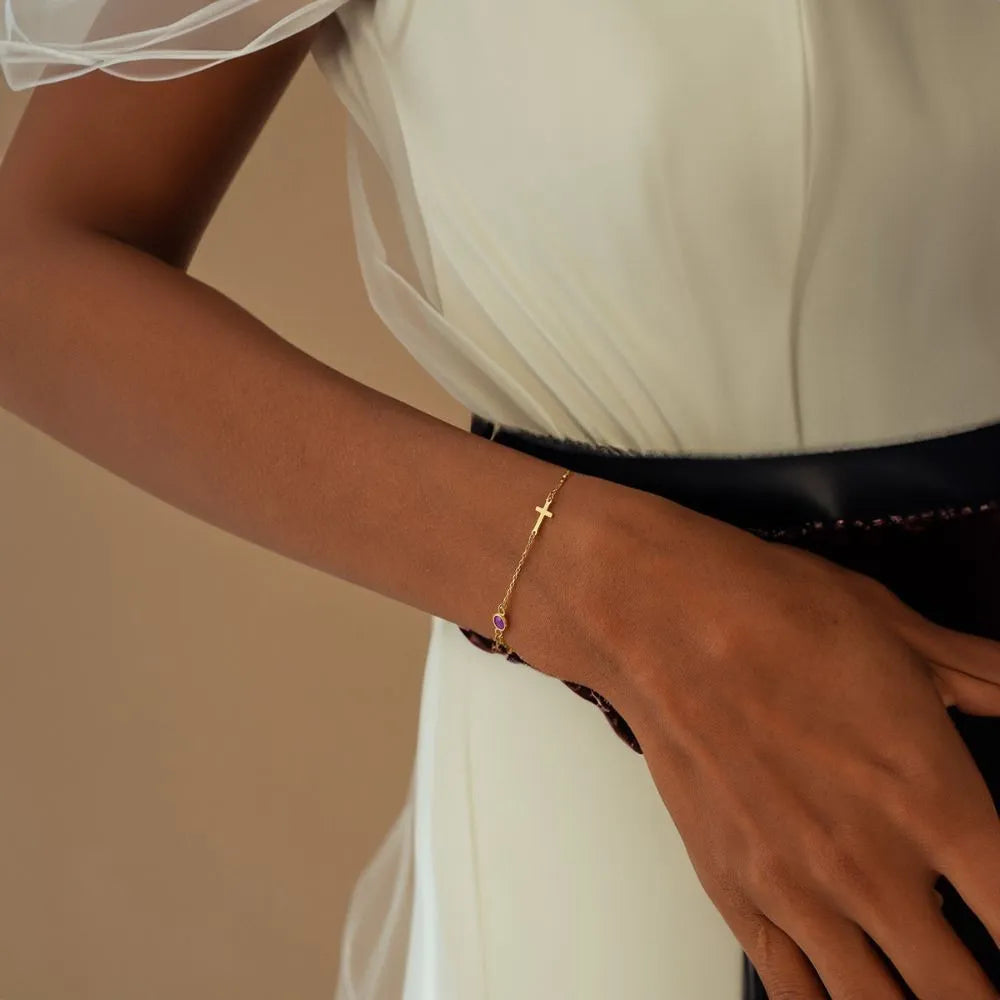 Close-up of a hand wearing a 14k gold bracelet with a pink gemstone against a neutral background