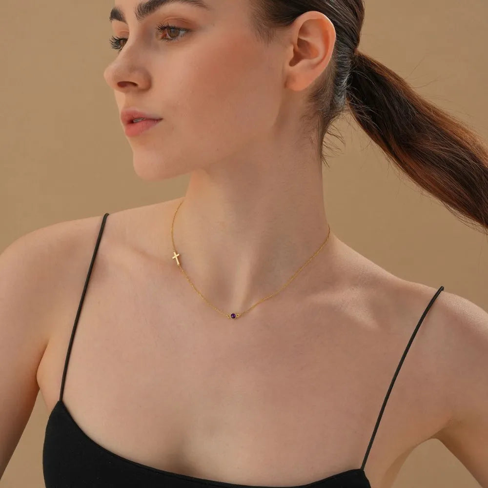 Woman wearing a delicate cross birthstone necklace against a neutral background