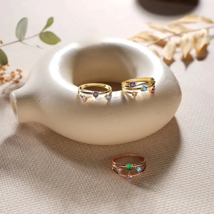 Three birthstone rings with colorful gemstones on a white ceramic dish.