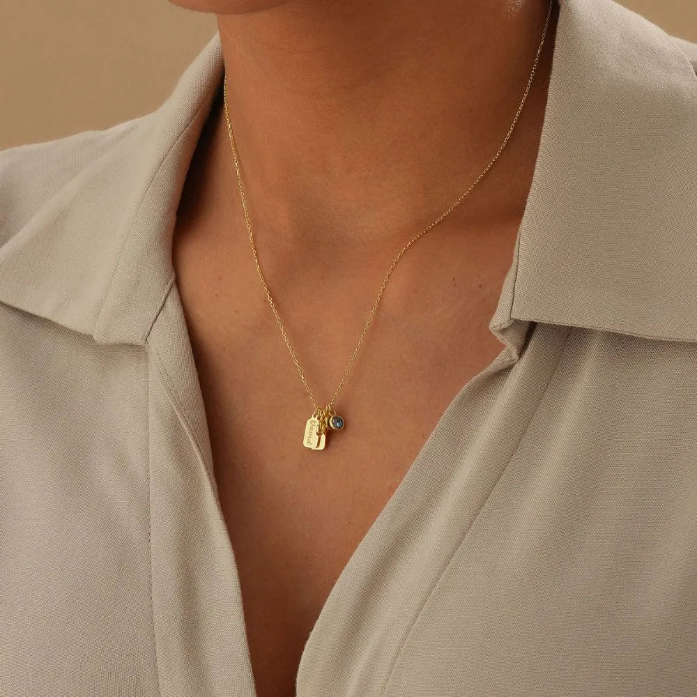 14k gold necklace with small pendants and birthstones worn by a person in a beige shirt.