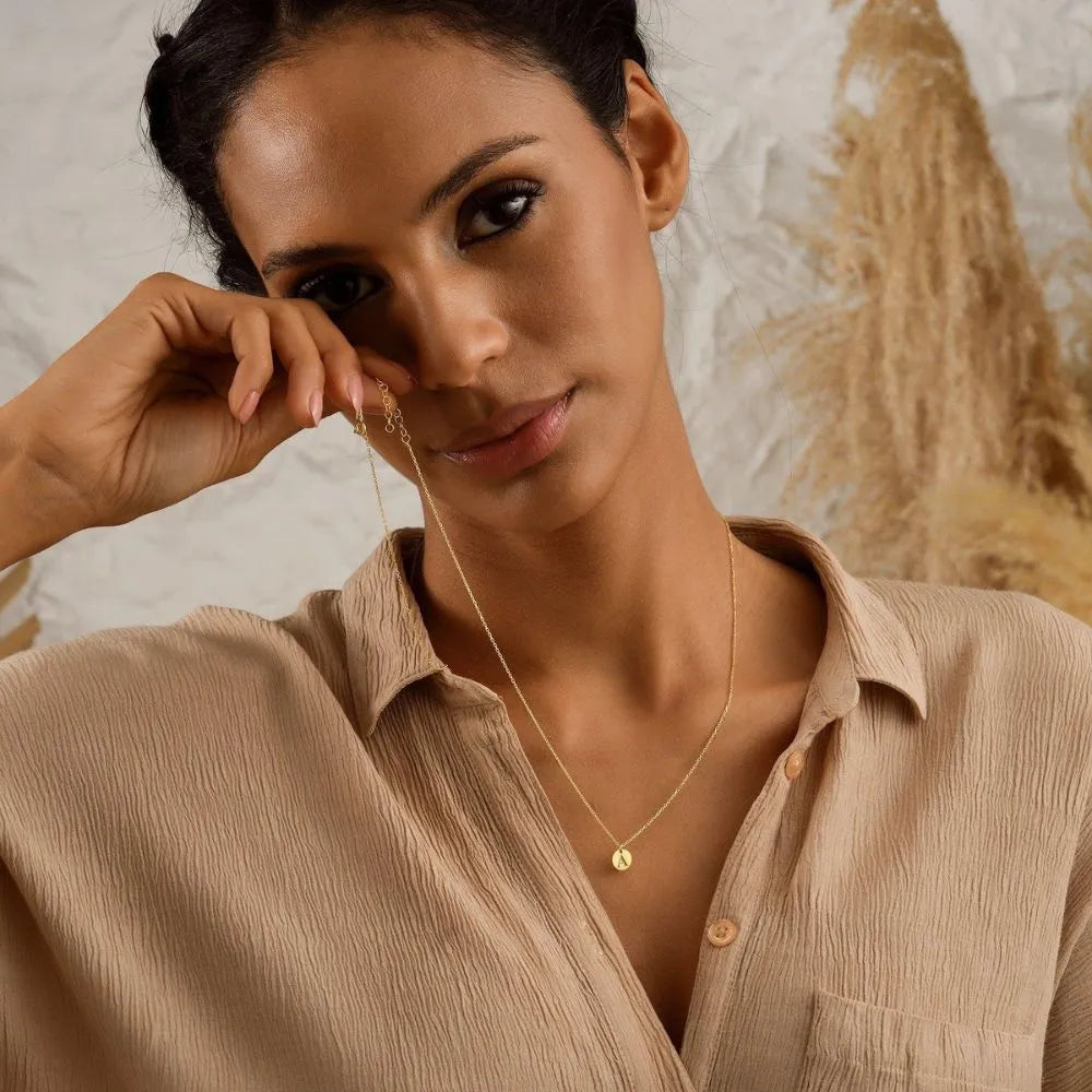 Woman wearing a tiny discs layer necklace against a neutral background