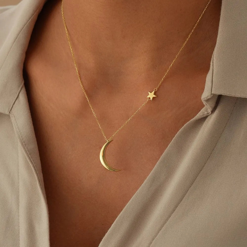 14k Gold necklace with a star and moon pendant on a person wearing a beige shirt.