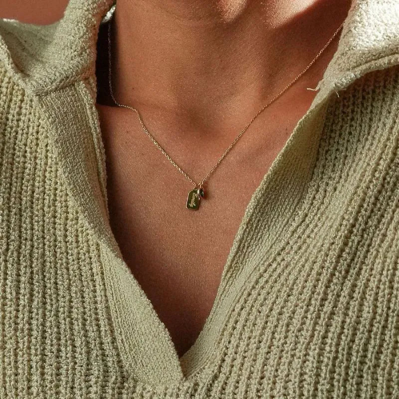 Close-up of a person wearing a 14k gold necklace with a name engraved pendant and birth month stone, set against a neutral background.