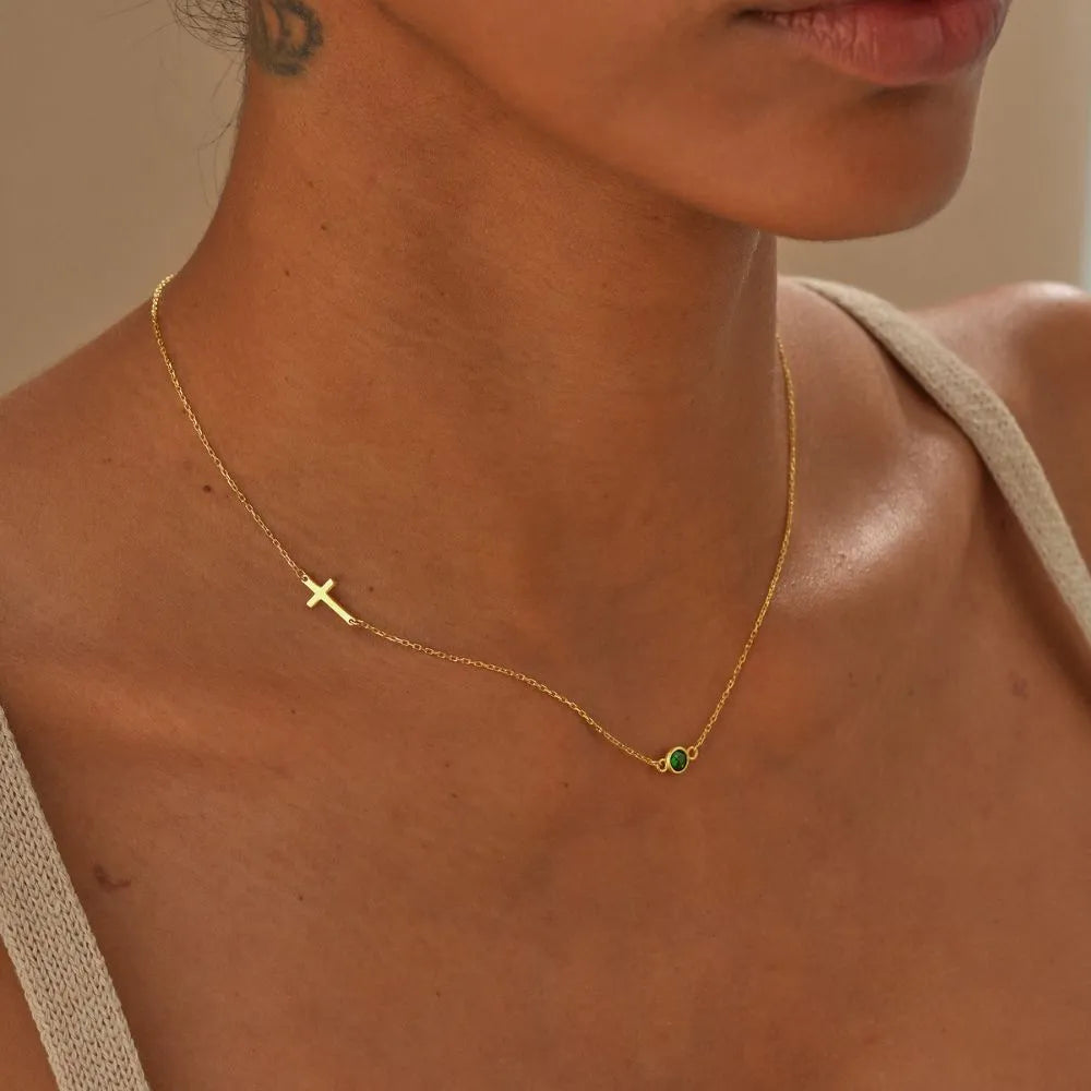 Close-up of a woman model wearing a 14k gold necklace with a cross pendant and birthstone gemstone.