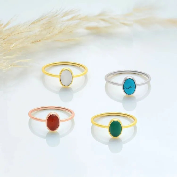Four oval natural stone rings with different colored stones on a light background.
Moonstone, Tuquoise, Carnelian, and Emerald.
