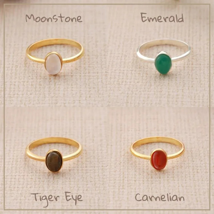 Four rings with different natural oval gemstones on a textured surface.
Natural stones:
Moonstone, Emerald, Tiger Eye, and Carnelian.
