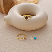 Two 14k gold filled rings with Tiger's Eye and Moonstone gemstones on a textured surface with a ceramic object in the background.