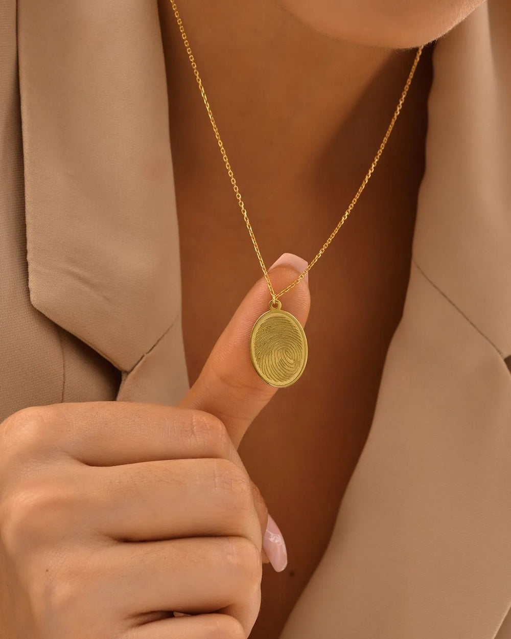 Gold necklace with a round pendant held by a hand against a brown background